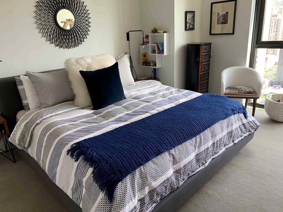 A made bed with a navy throw and white pillows, lit by a corner window