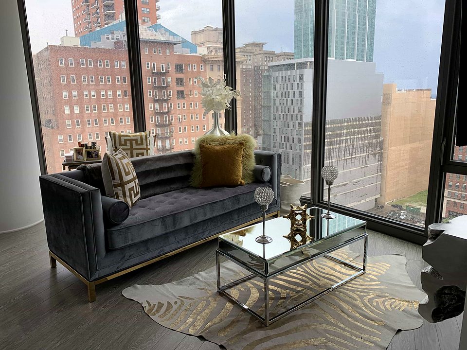 A grey velvet sofa and mirrored coffee table in a downtown high-rise, with floor-to-ceiling windows over the city